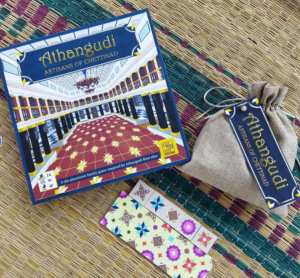 The board game box for Athangudi: Artisans of Chettinad by XOtoXO Games, shown with its cloth pouch and colorful floor-tile cards